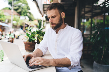 Focused freelancer in street cafe working on laptop with full attention. Concept of deep tech concentration, minimal distraction and precision-driven freelance performance in remote settings.