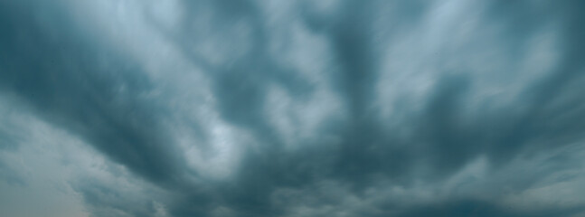 Thick, dark storm clouds swirl and stretch across the sky in a dramatic display, creating a moody...