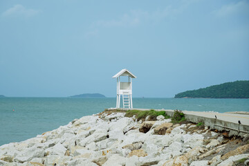 Small lighthouse on the shore of the sea at Khao Laem Ya, Rayong, Thailand. Little wooden white life guard tower. Summer travel vacation and holiday concept. Seascape Bridge and Pier.