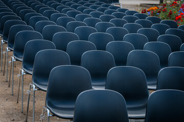 Fototapeta premium Multiple rows of identical black chairs are neatly arranged in an outdoor setting on a dirt surface, creating a uniform and symmetrical pattern.