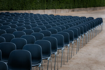 Multiple rows of identical black chairs are neatly arranged in an outdoor setting on a dirt...