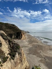 Warm coastal beach with rocky cliffs and a serene ocean view during a cloudy afternoon