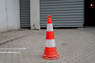 Traffic safety cone on paved surface in front of closed industrial garage door symbolizing...