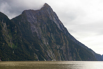 dramatic landscape of Milford Sound, powerful Falls cascading from mountain cliffs during heavy...