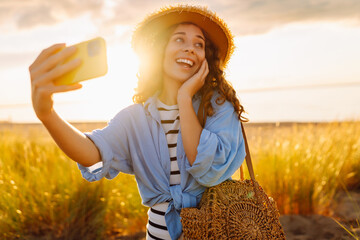 Selfie time! Happy woman on the beach with a phone enjoying the sunset on the beach. Young tourist...