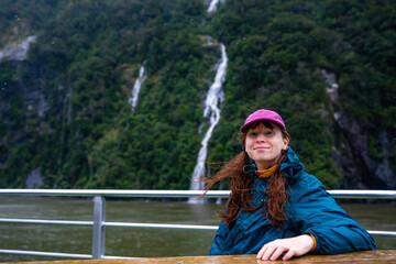 girl smiles as she admires a wall of numerous waterfalls cascading down a dramatic mountain cliff...
