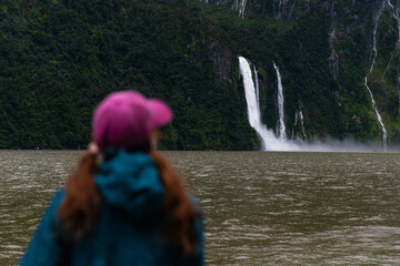 girl smiles as she admires a wall of numerous waterfalls cascading down a dramatic mountain cliff...
