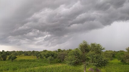 Brooding monsoon clouds roll over a lush green landscape, capturing nature’s raw tension before...
