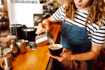 A barista in an apron prepares coffee using a coffee machine behind the bar. An experienced barista...