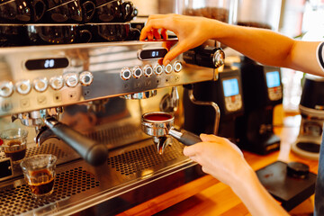A barista in an apron prepares coffee using a coffee machine behind the bar. An experienced barista...