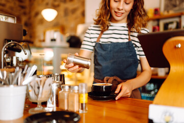 A barista in an apron prepares coffee using a coffee machine behind the bar. An experienced barista...