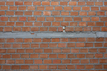 A partially constructed red brick wall with visible grey mortar and steel reinforcing bars (rebar), indicating