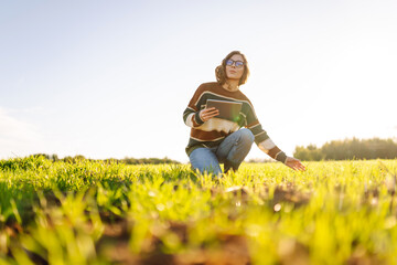 Young female agronomist with a digital tablet works on a green agricultural field. Female farmer checks young sprouts and the quality of the harvest using modern technology. Farming,  technology conce