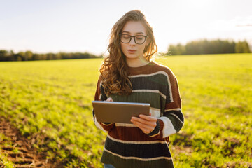 Young female agronomist with a digital tablet works on a green agricultural field. Female farmer...
