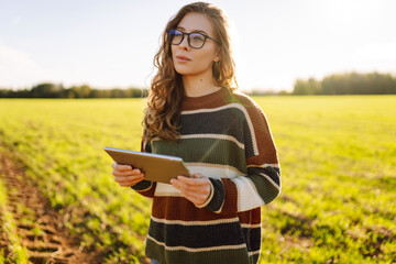 Young female agronomist with a digital tablet works on a green agricultural field. Female farmer...