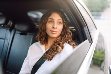 Happy woman with curly hair in the backseat of a car with a phone looks out of the car window....