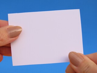 Obraz premium Closeup of woman hands holding a blank white card on blue background. Hands holding blank card.