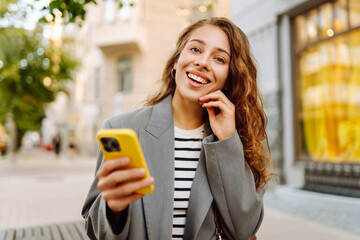 Portrait of a happy woman with a phone in her hands walking along the streets of the city. A...