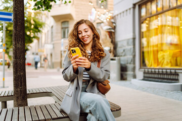 Portrait of a happy woman with a phone in her hands walking along the streets of the city. A...