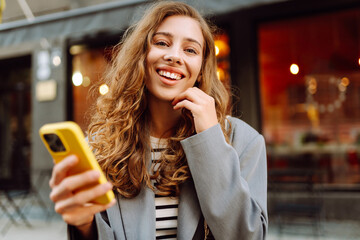 Portrait of a happy woman with a phone in her hands walking along the streets of the city. A...