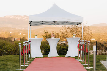 Elegant outdoor event setup with white tent and red carpet at sunset in picturesque landscape	