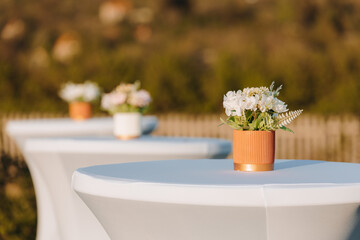 Beautiful floral arrangements adorn cocktail tables at an outdoor event during sunset	