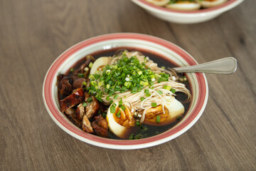 Ramen. A flavorful bowl of noodles features tender chicken, sliced boiled eggs, and fresh green onions in a savory broth. Served in a warm kitchen, it's a perfect comfort meal