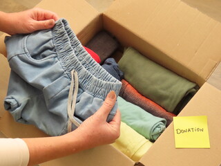 Woman hands preparing a box of clothes for donation. Hands holding a child short. Sorting clothes...
