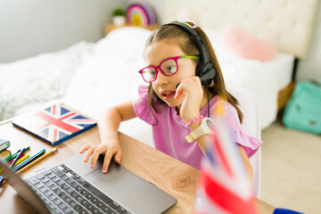 Tween girl learning english online with a laptop and headphones