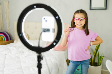 Influencer tween making peace sign while recording content with ring light