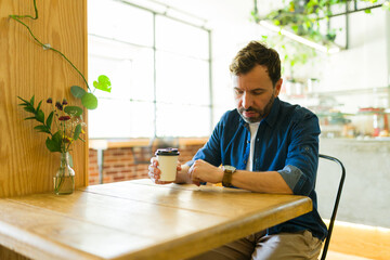 Latin man checking time while waiting in cafe