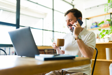 Freelancer working remotely in coffee shop, enjoying coffee and talking on phone
