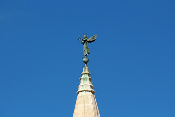 A bronze angel statue with outstretched wings and a halo stands on a globe at the pinnacle of a...