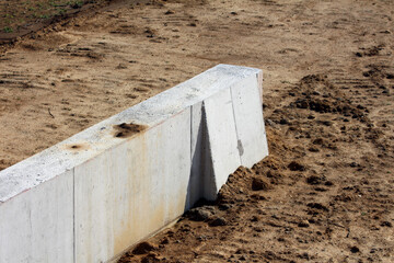 A sturdy, angular concrete barrier stands firmly in the middle of a sandy, uneven construction...