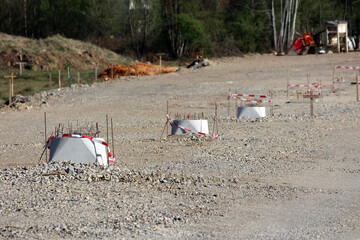 Multiple concrete foundation pillars with protruding steel rebar are spaced evenly across a leveled...