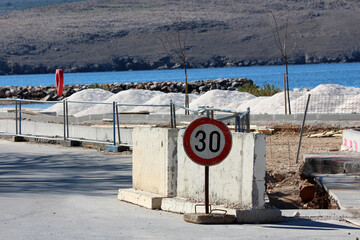 A weathered concrete barrier with a faded 30 km/h speed limit sign stands on a seaside road,...
