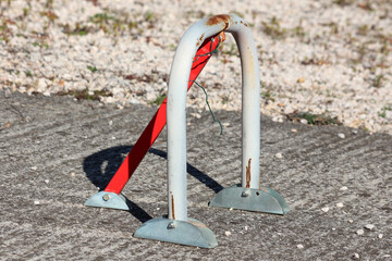 A sturdy metal U-shaped parking barrier with a red diagonal support is anchored to a concrete...