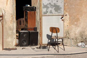 A collection of vintage wooden speakers, amplifiers, and black subwoofers sits outside a worn,...