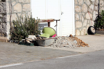 A heap of broken concrete, bricks, and an upturned green toilet bowl lies beside a stone house and...