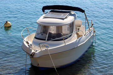 A compact white motorboat with a solar panel mounted on its roof floats on calm, clear blue water,...