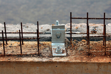 A galvanized steel anchor bracket is bolted to a concrete beam, surrounded by exposed and rusted...
