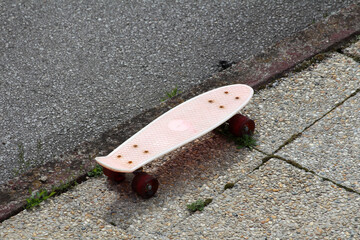 A small pink skateboard with red wheels and a textured deck rests abandoned at the edge of a...