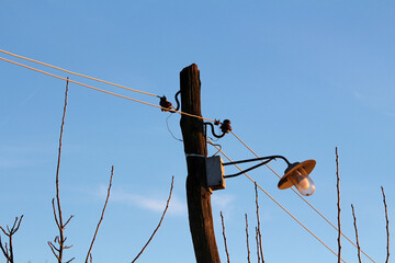A tall, dark wooden utility pole supports a classic metal street lamp with a conical shade and...