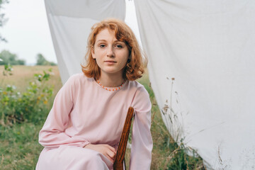 Redhead Girl in Pink Dress Sitting on Chair in the Field