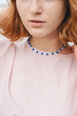 Close-up of handmade blue beaded necklace on young woman in pink dress