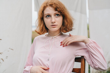 Redhead Woman in Pink Dress Touching Collar While Sitting Outdoors