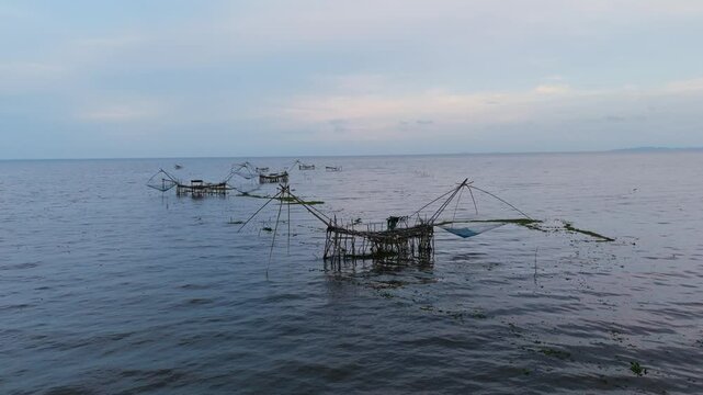 Traditional bamboo fishing nets in a calm lake at dusk. Peaceful rural scene capturing local fishing lifestyle in Southeast Asia. Ideal for travel, nature, and cultural content.
