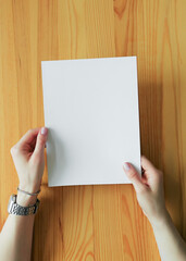Hands Holding a Blank White Paper on a Wooden Surface