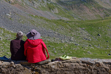 Back of two unrecognizable old hikers sitting in front of green alp slopes