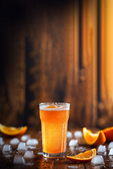 A refreshing glass of juicy orange soda served over ice cubes on a wooden table background, Bright and fizzy orange soda in a clear glass with ice cubes placed on a wooden table.